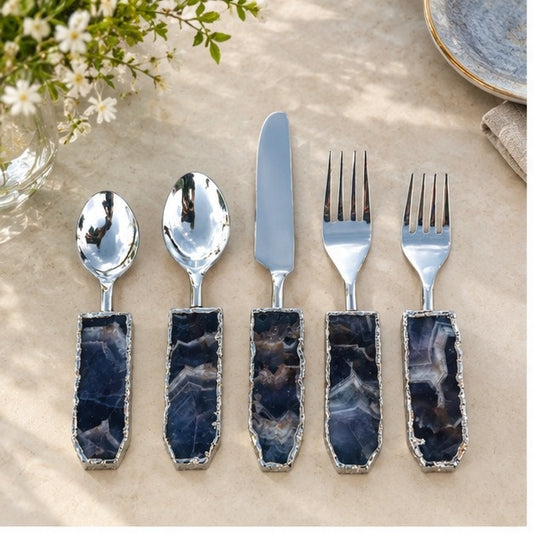 Amethyst agate cutlery set of five with deep purple stone handles and silver edges, on pale stone