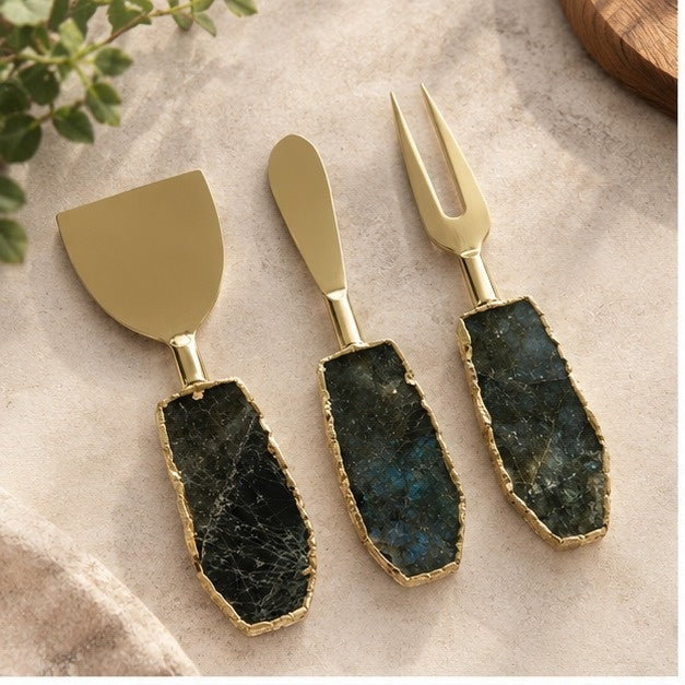 Labradorite cheese knife set of three with gold blades and dark stone handles, on cream linen