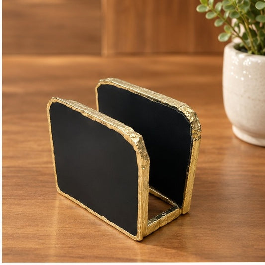Black agate napkin holder with a gold electroformed edge, on a wood table beside a plant