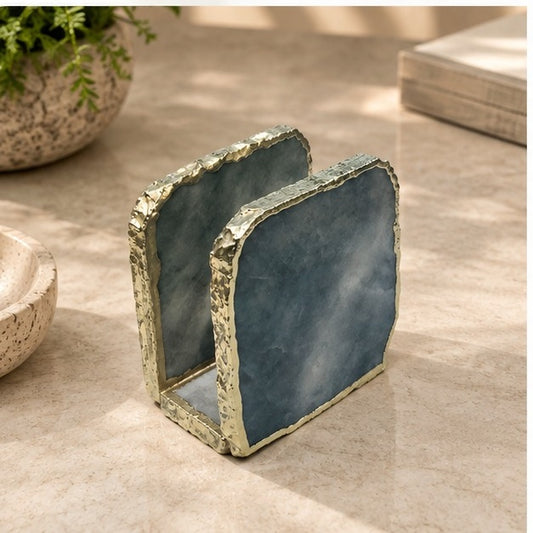 Grey agate napkin holder with a gold electroformed edge, on marble beside books and a plant