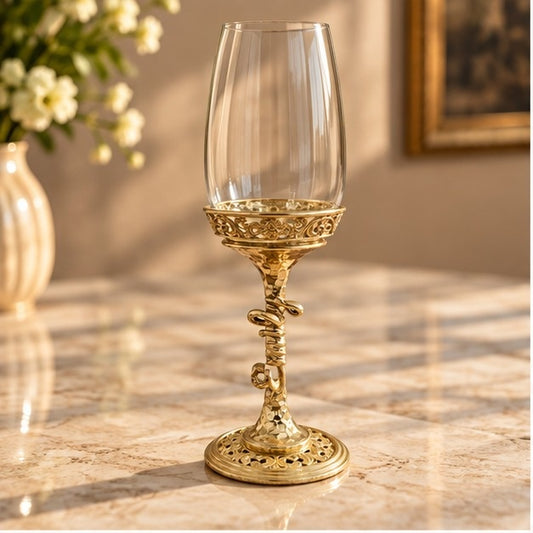 The Helix wine glass, clear bowl on a gold spiral stem, on marble beside white blossom