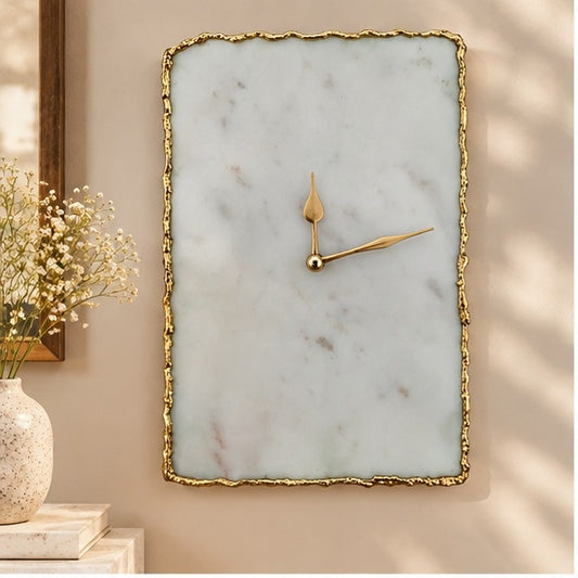 Large white marble wall clock with a gold organic edge, on a warm wall beside dried blossom