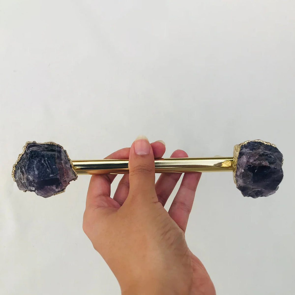 Hand holding the gold rod, purple crystal ends catching the light