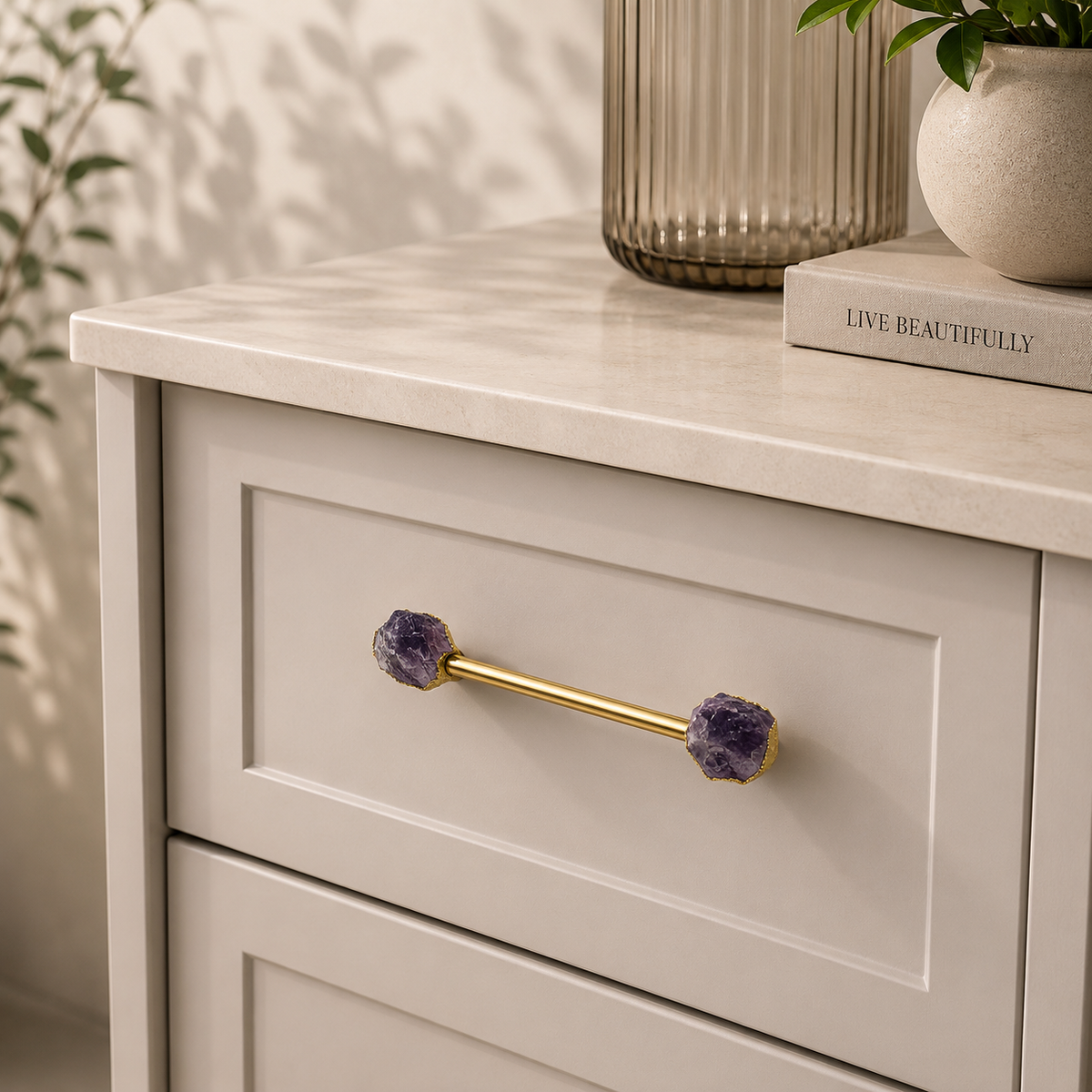 Amethyst tipped bar pull in gold on a cream drawer, fluted vase above