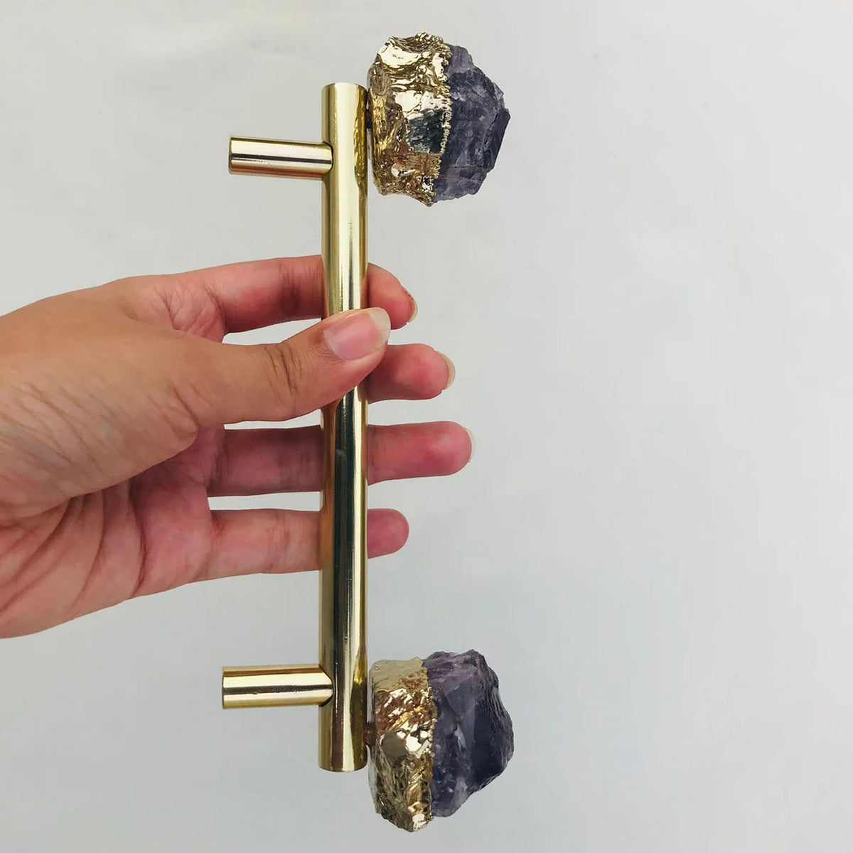 Gold bar pull upright in a hand, amethyst caps top and bottom