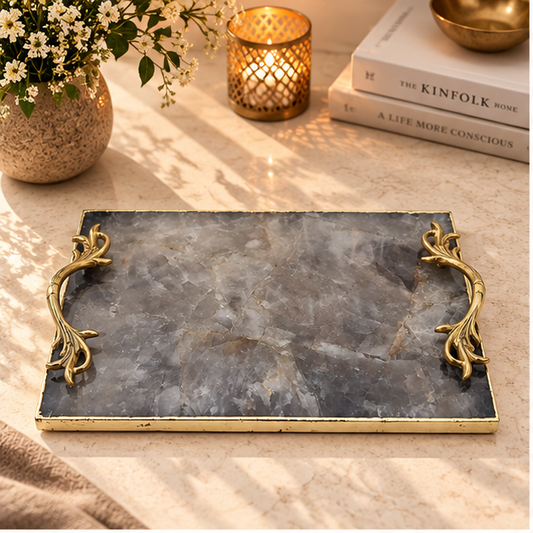 Smoky quartz rectangular tray with ornate gold leaf handles, on a counter with candles and books