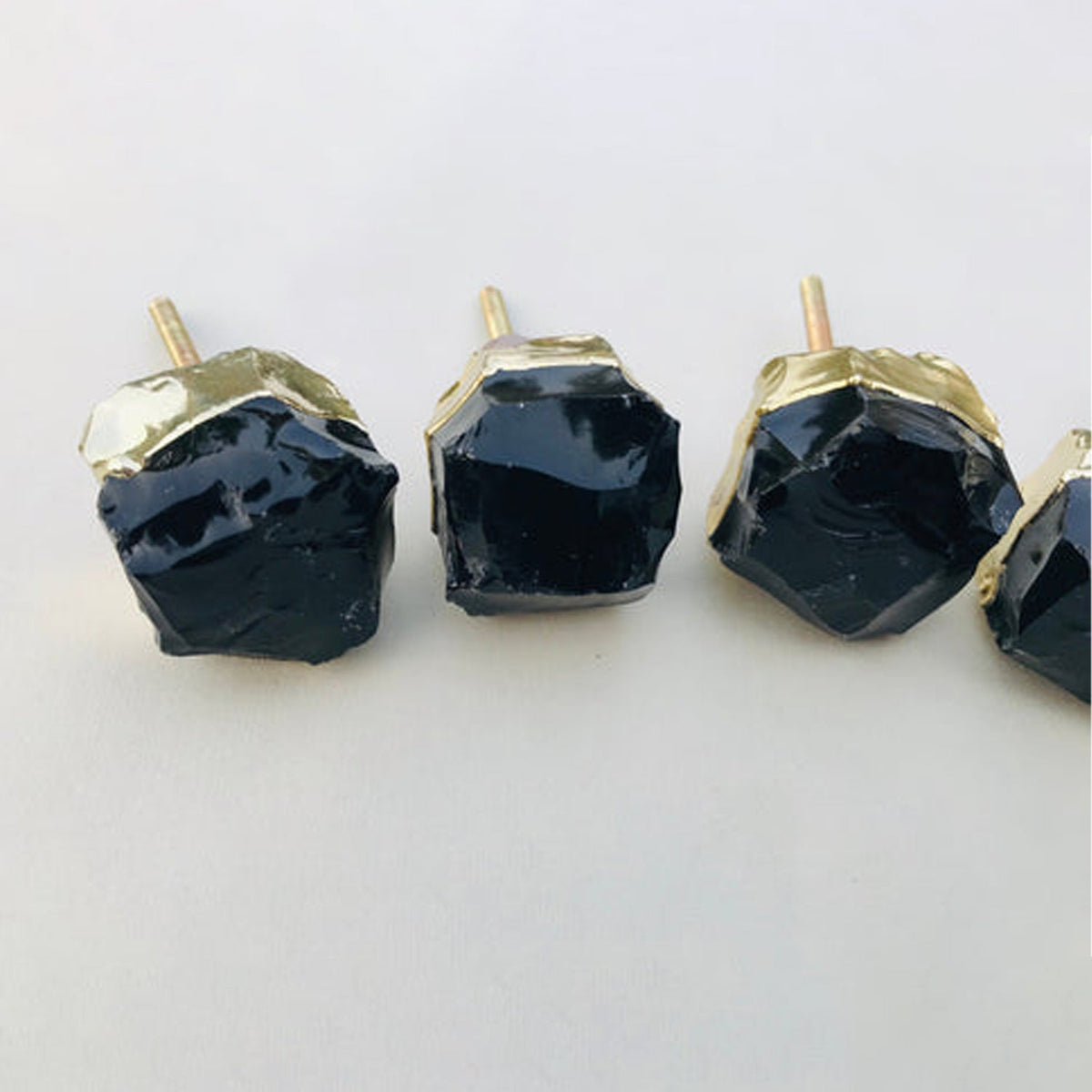 Four raw obsidian knobs in a row, glassy black facets in gold caps