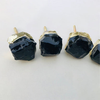 Four raw obsidian knobs in a row, glassy black facets in gold caps