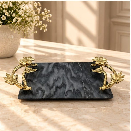 Black marble tray with large gold floral handles, on a counter beside white blossom