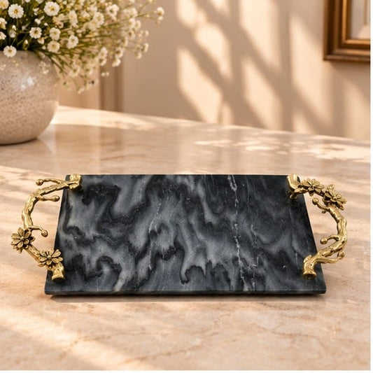 Black marble tray with small gold floral handles, on a counter beside white blossom