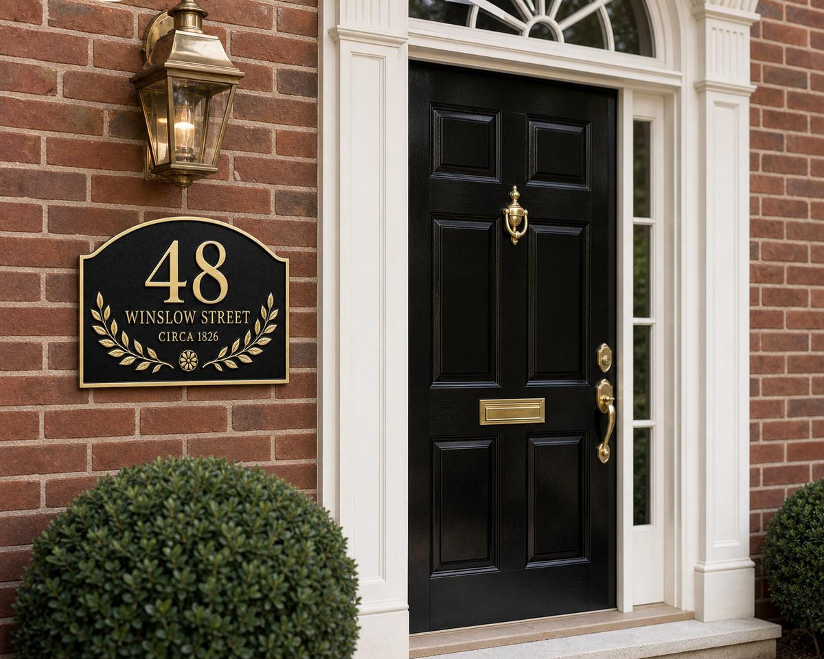 Arched Laurel plaque pictured on brickwork beside a black panelled door