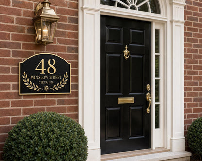 Arched Laurel plaque pictured on brickwork beside a black panelled door